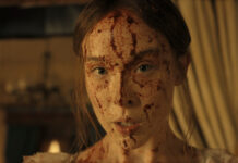Un coup de hache dans le catalogue Netflix : Lizzie Borden est la nouvelle Monster "A young woman with long hair, dressed in light clothing, has her face and upper chest covered in blood, standing indoors with dim warm lighting and blurred curtains and furnishings in the background."