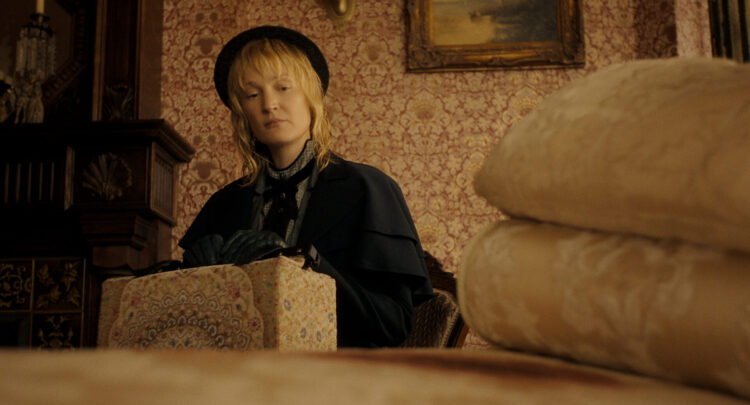 Un coup de hache dans le catalogue Netflix : Lizzie Borden est la nouvelle Monster 2 "A woman in vintage clothing and gloves sits indoors, holding a patterned box. The room has ornate wallpaper, a painting, and folded linens in the foreground, suggesting a historical or period setting."